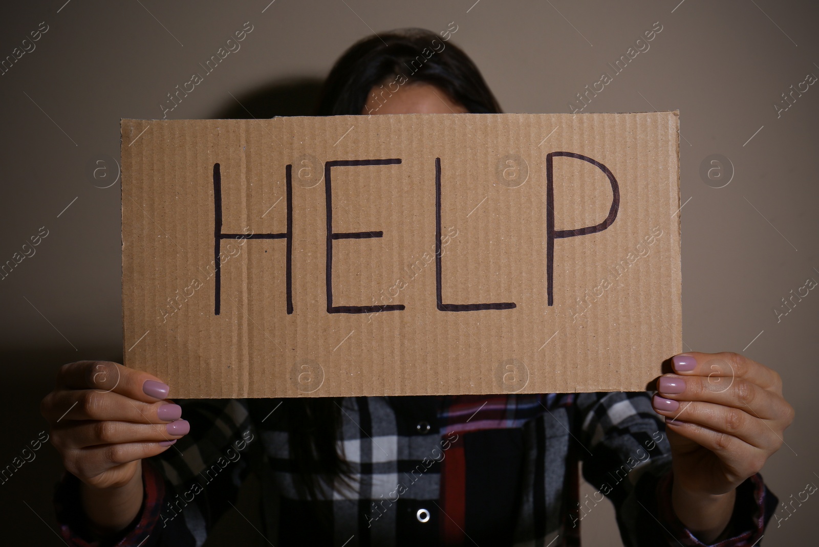 Photo of Young woman with sign HELP near beige wall. Domestic violence concept