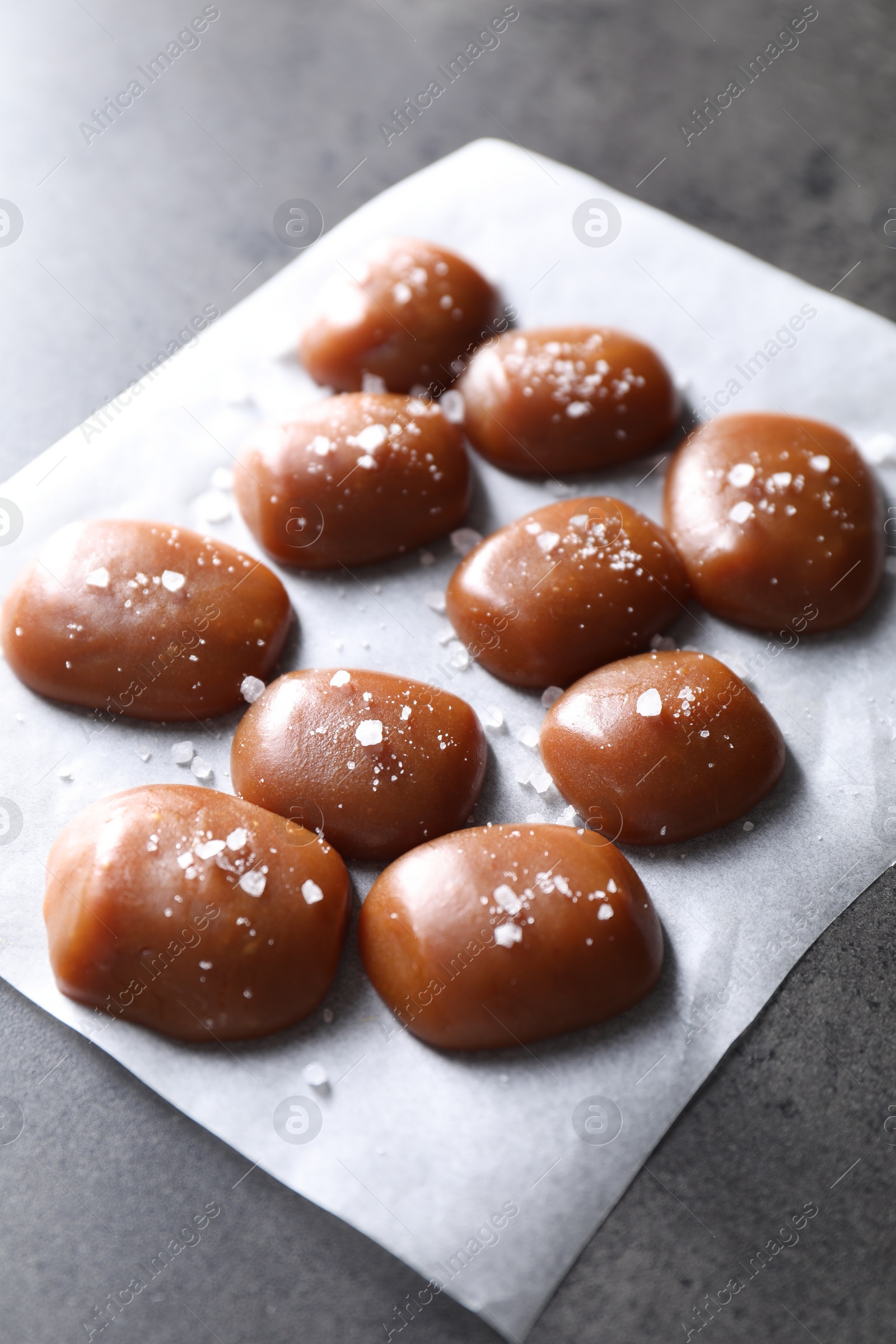 Photo of Tasty caramel candies and salt on grey table