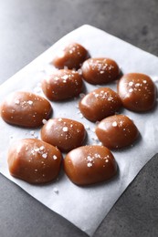 Tasty caramel candies and salt on grey table