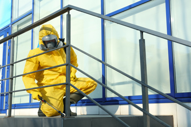 Photo of Male worker in protective suit spraying insecticide on stairs outdoors. Pest control