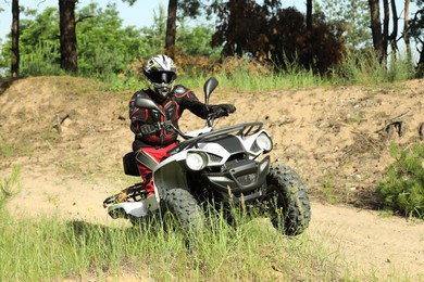 Man driving modern quad bike on sandy road near forest. Extreme sport