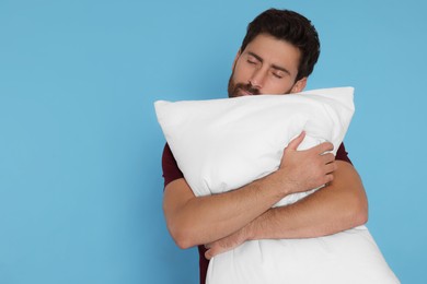 Sleepy handsome man hugging soft pillow on light blue background, space for text