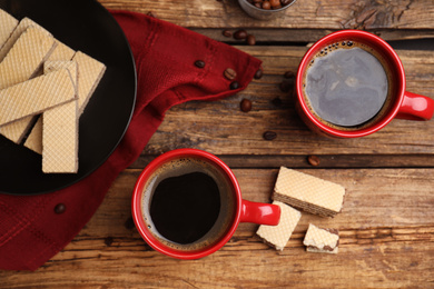 Delicious wafers and coffee for breakfast on wooden table, flat lay