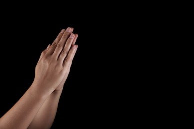 Photo of Woman holding hands clasped while praying on black background, closeup. Space for text