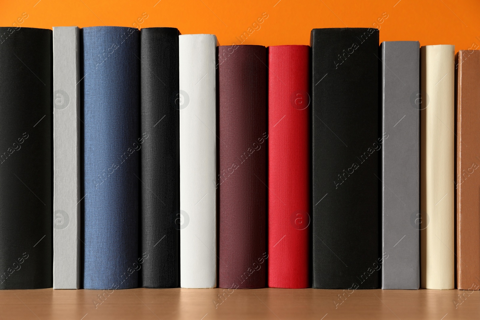 Photo of Many books on wooden table near orange wall, closeup