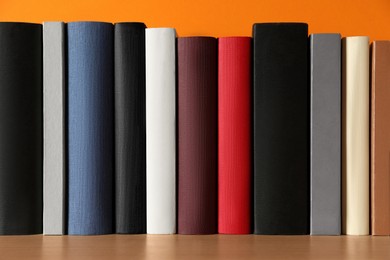 Photo of Many books on wooden table near orange wall, closeup