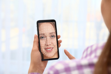Woman using smartphone with facial recognition system on blurred background, closeup. Biometric verification