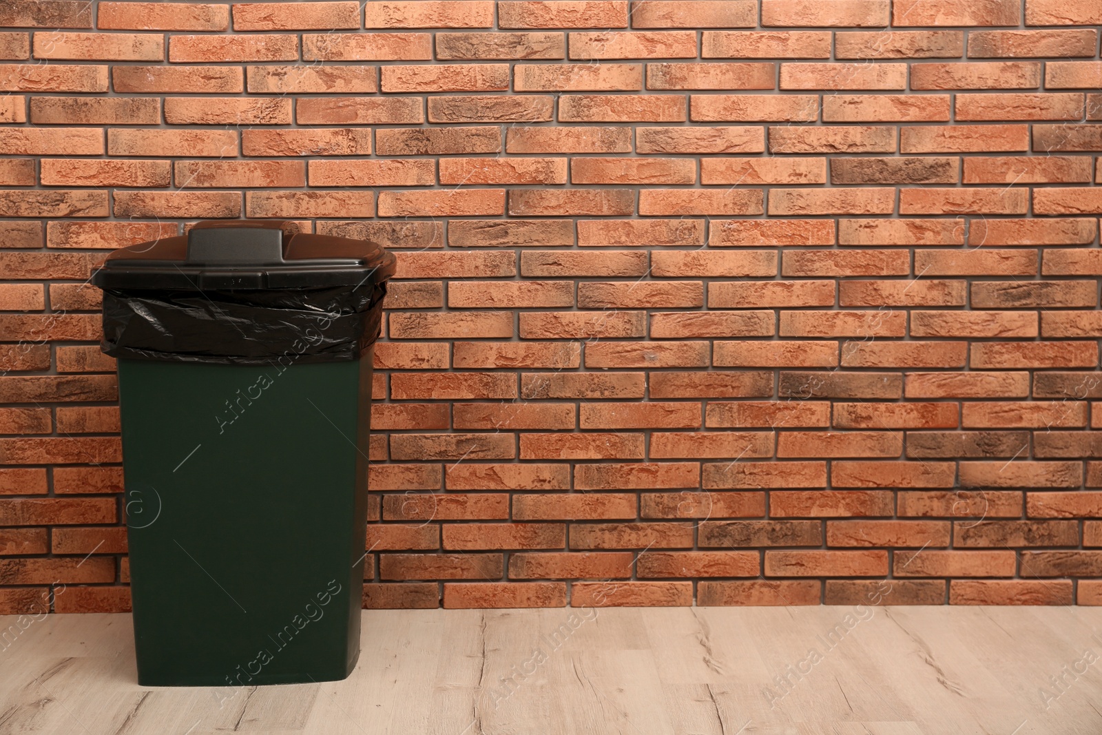 Photo of Closed trash bin near brick wall indoors, space for text. Waste recycling