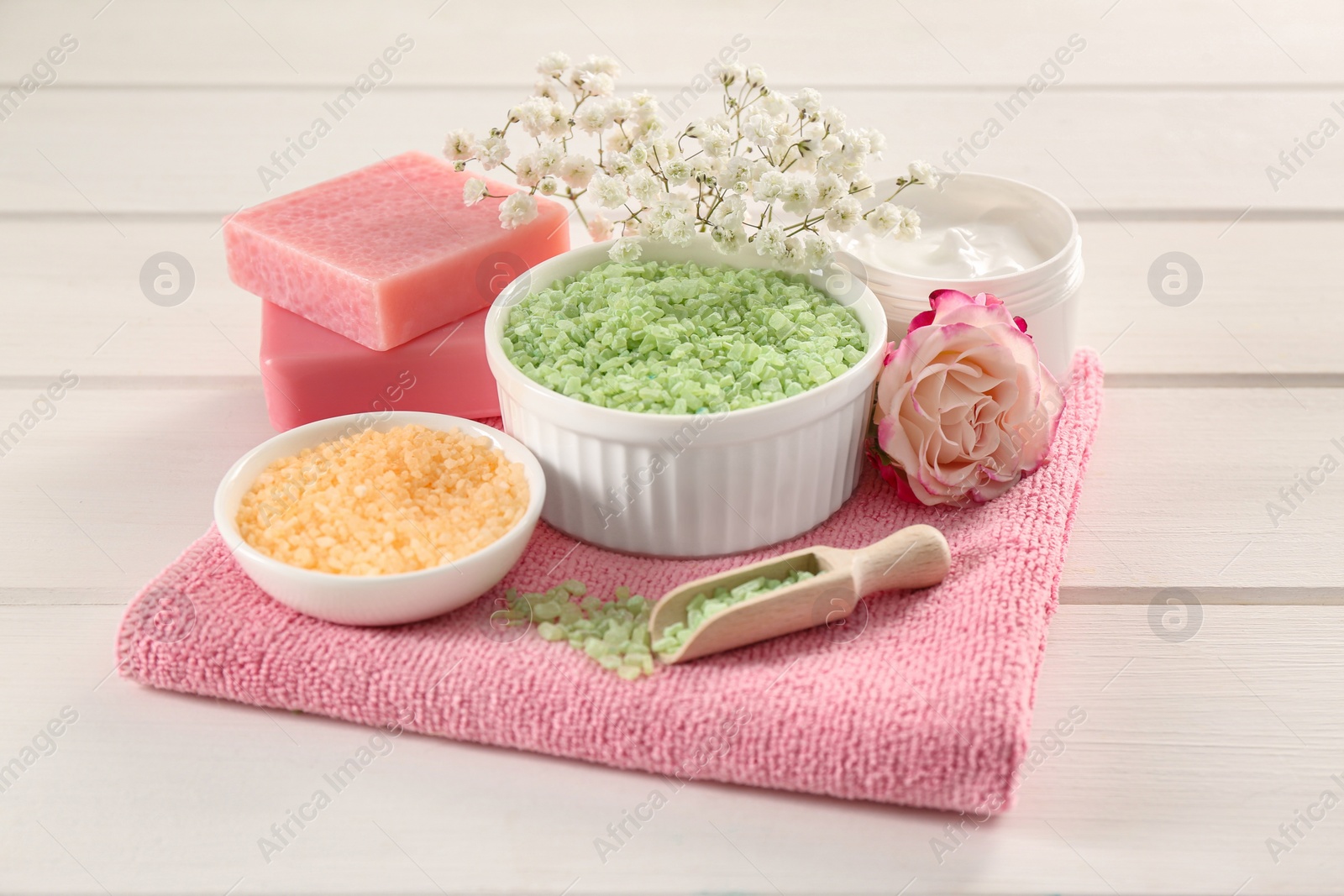 Photo of Bowls with sea salt, beautiful rose and soap bars on white wooden table