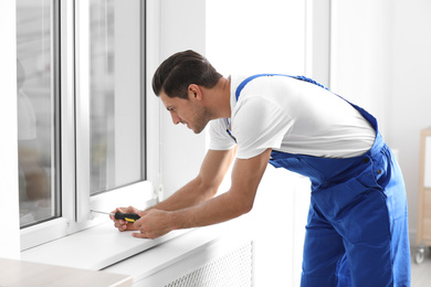 Construction worker repairing plastic window with screwdriver indoors