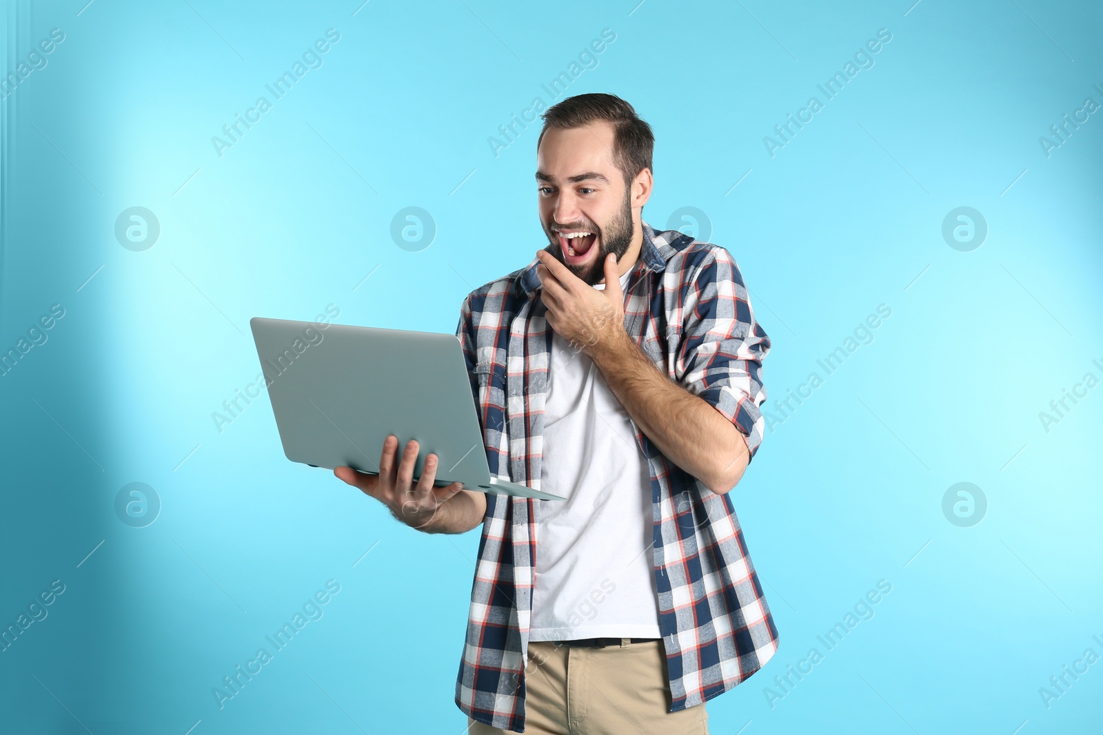 Photo of Emotional young man with laptop celebrating victory on color background