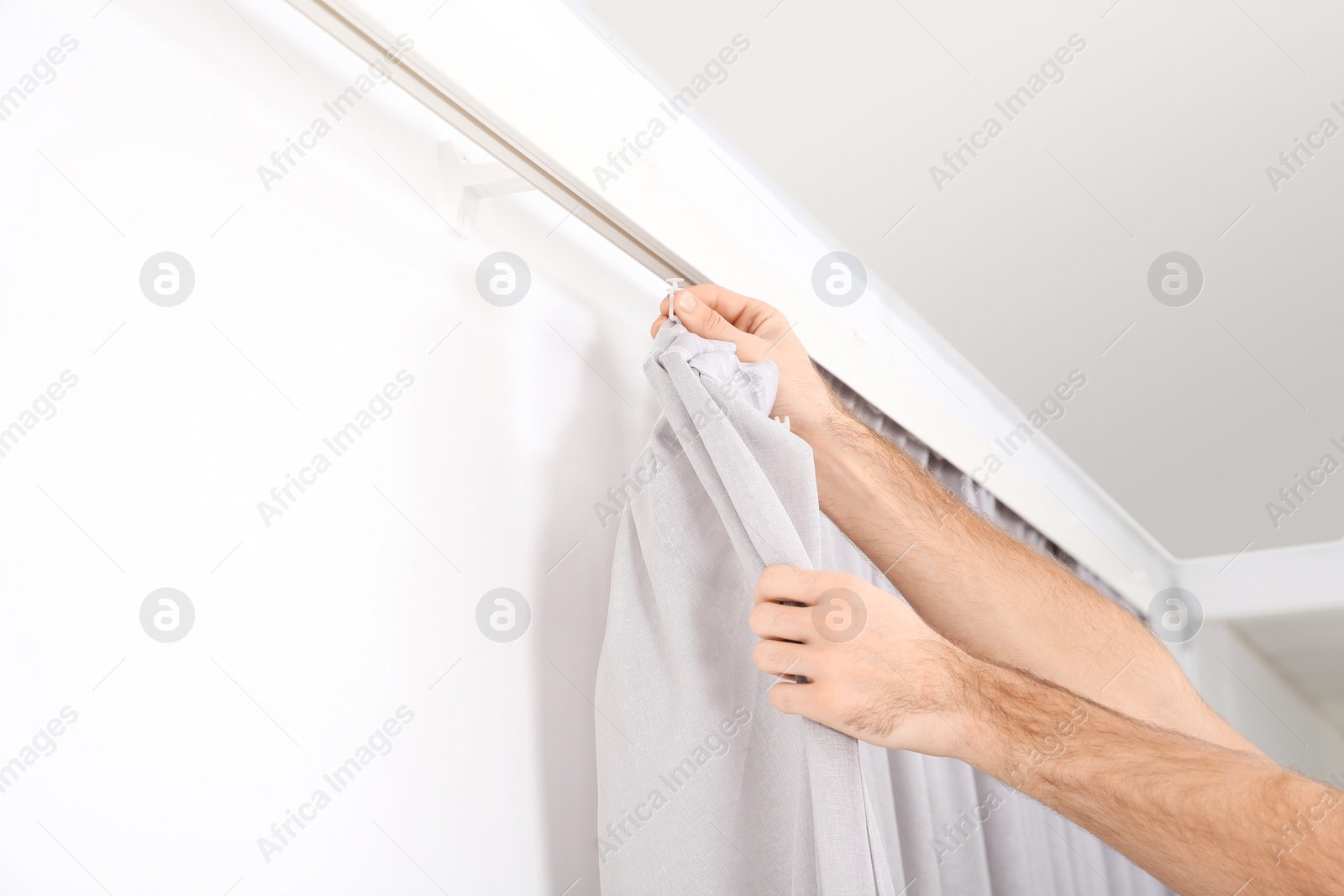Photo of Man hanging window curtain indoors, closeup. Interior decor element
