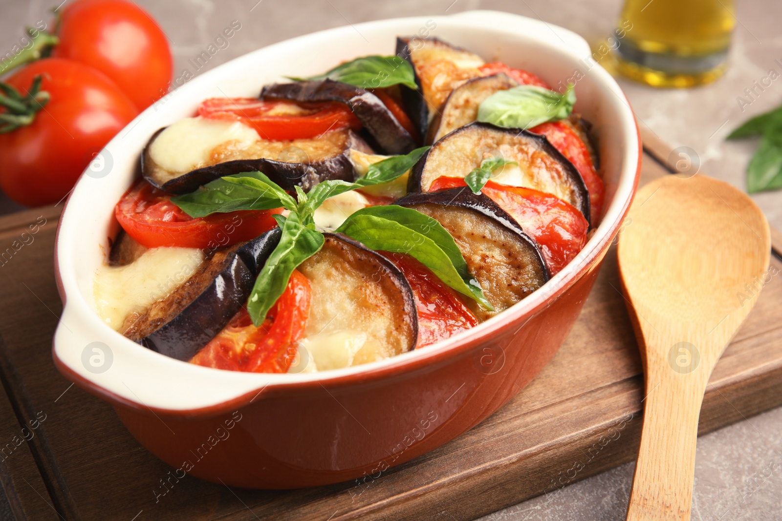 Photo of Baked eggplant with tomatoes, cheese and basil in dishware on cutting board