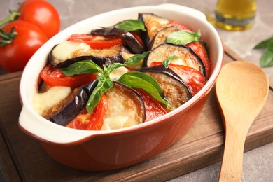 Photo of Baked eggplant with tomatoes, cheese and basil in dishware on cutting board