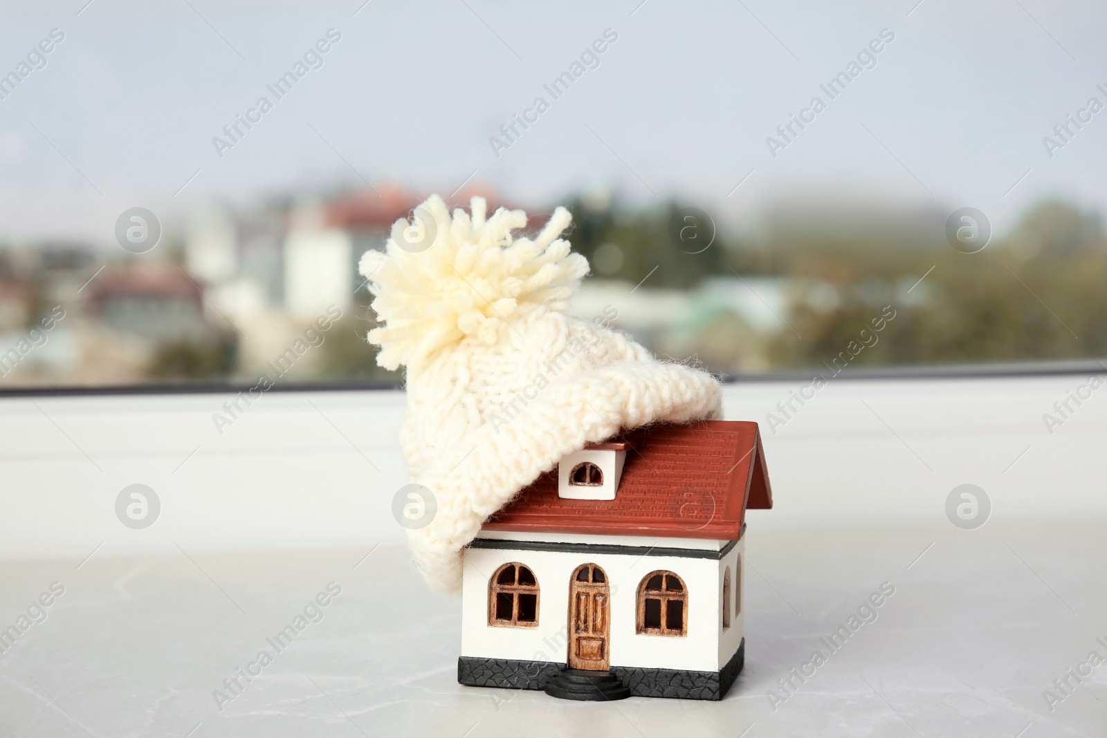 Photo of House model with knitted hat on table against blurred background. Heating concept