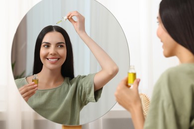 Photo of Beautiful woman applying hair serum in room. Cosmetic product