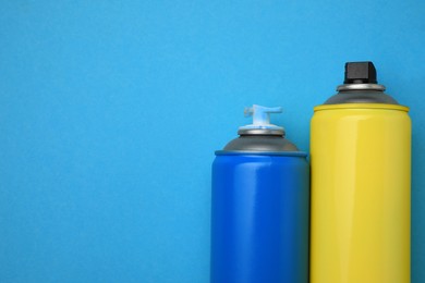 Cans of different graffiti spray paints on light blue background, flat lay. Space for text