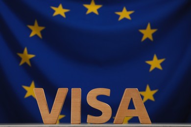 Photo of Word Visa made of wooden letters on table against European Union flag. Space for text