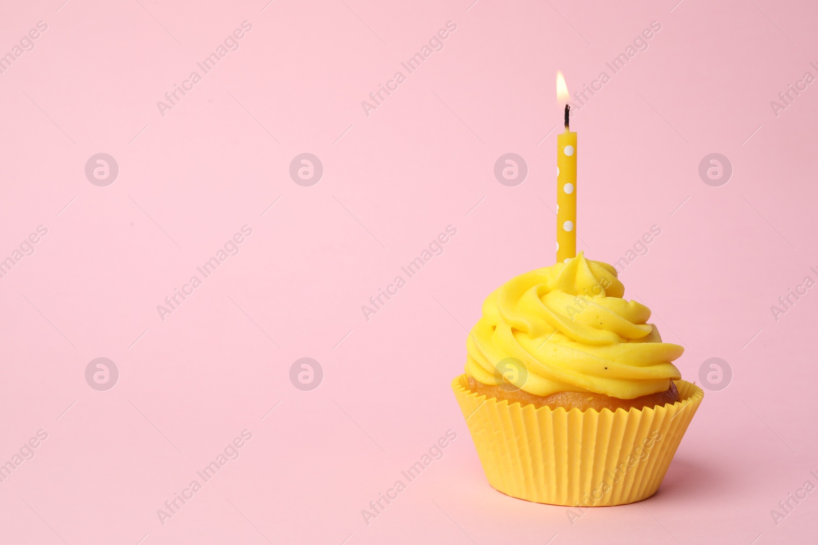 Photo of Delicious birthday cupcake with yellow cream and burning candle on pink background. Space for text