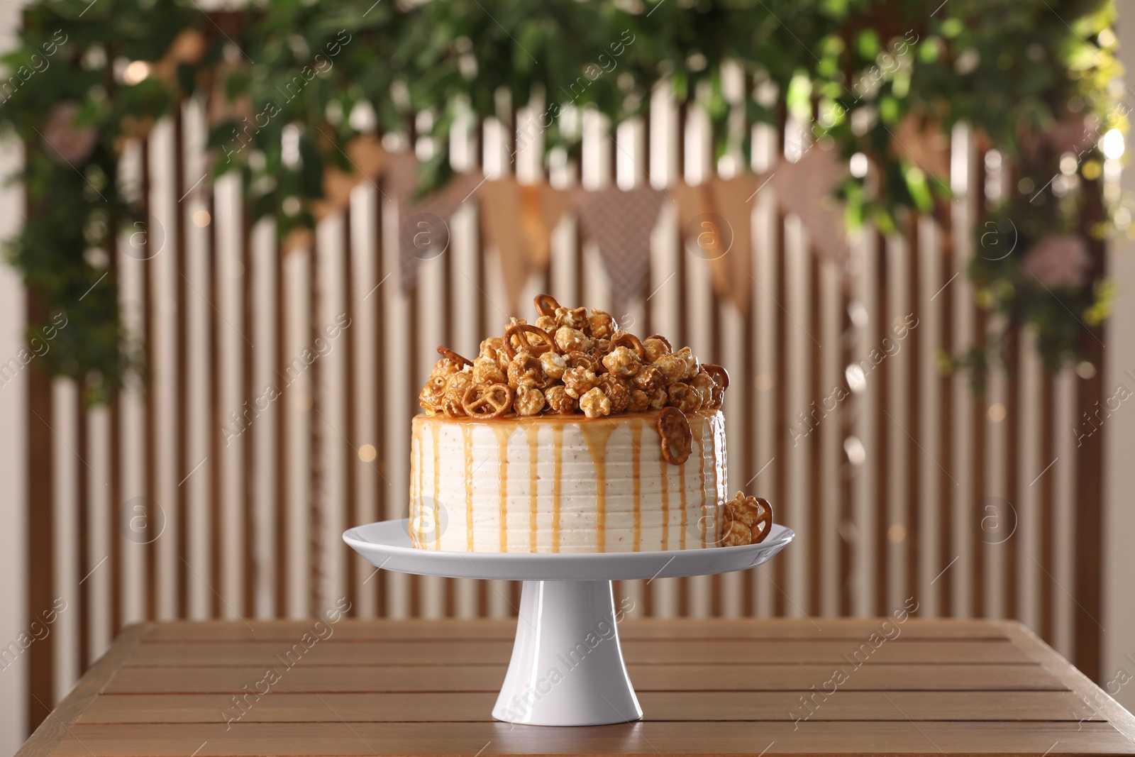 Photo of Caramel drip cake decorated with popcorn and pretzels on wooden table