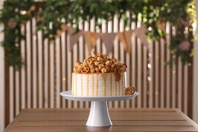 Photo of Caramel drip cake decorated with popcorn and pretzels on wooden table