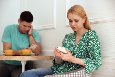 Photo of Man and young woman preferring smartphones over speaking with each other during first date in cafe