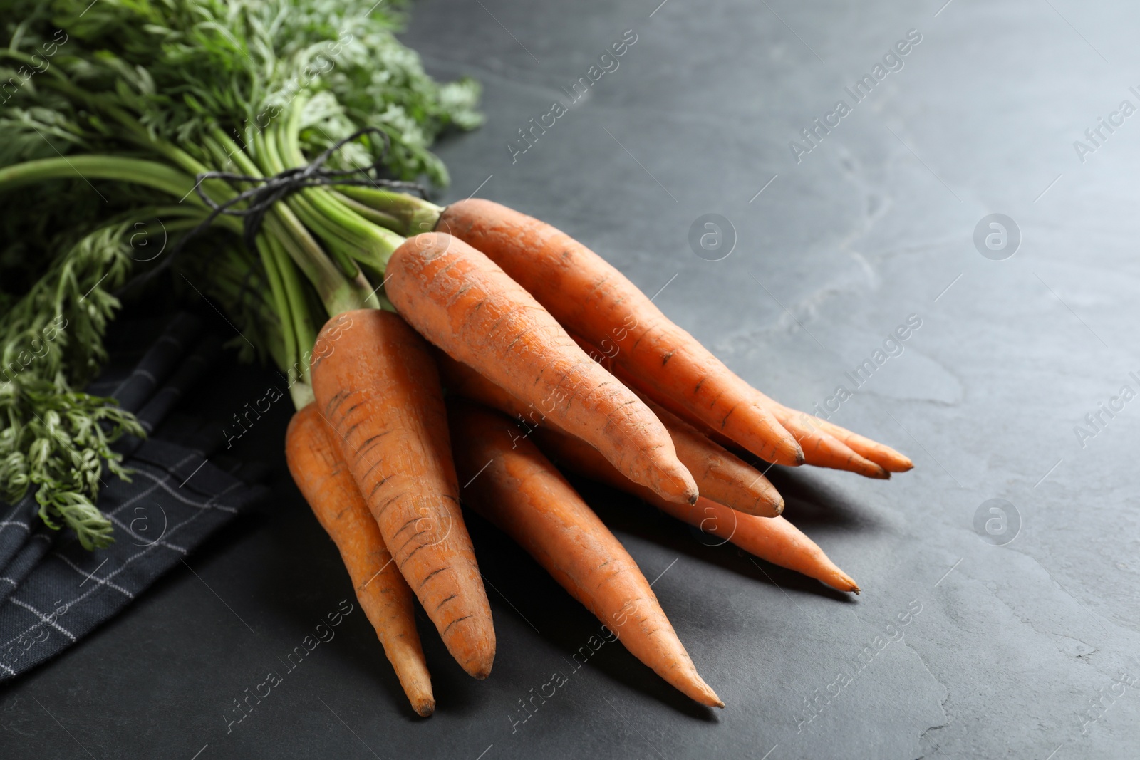 Photo of Bunch of tasty raw carrots on black slate table, closeup