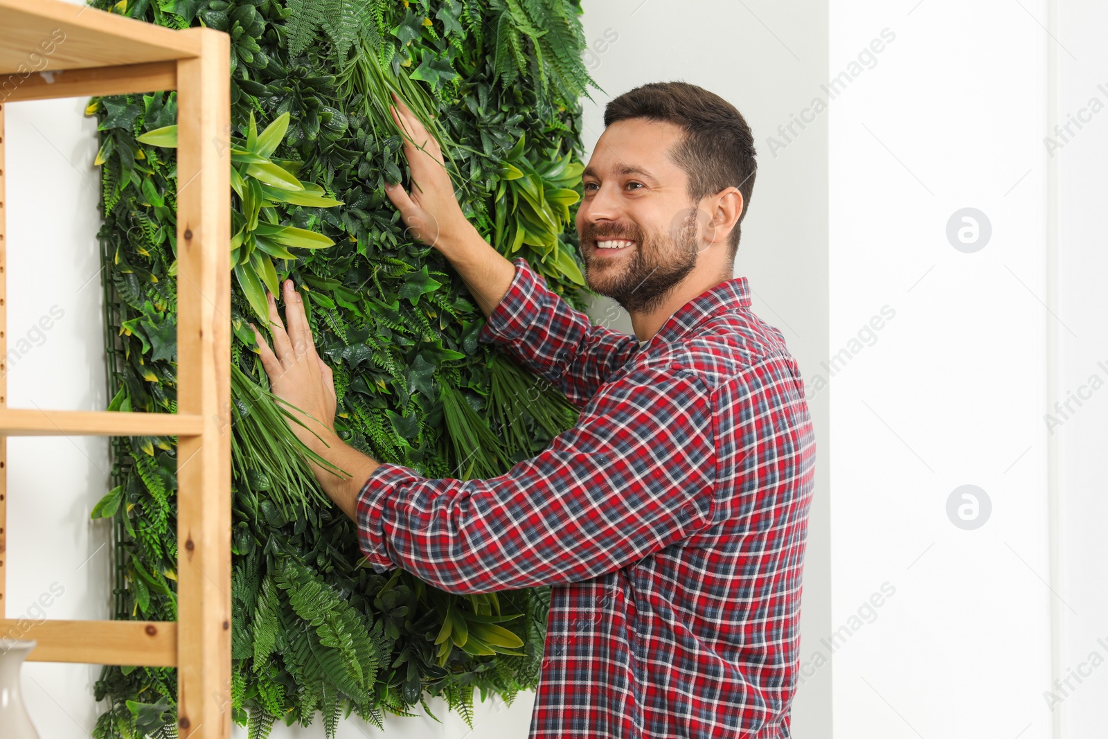 Photo of Man installing green artificial plant panel on white wall in room