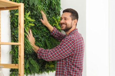 Man installing green artificial plant panel on white wall in room