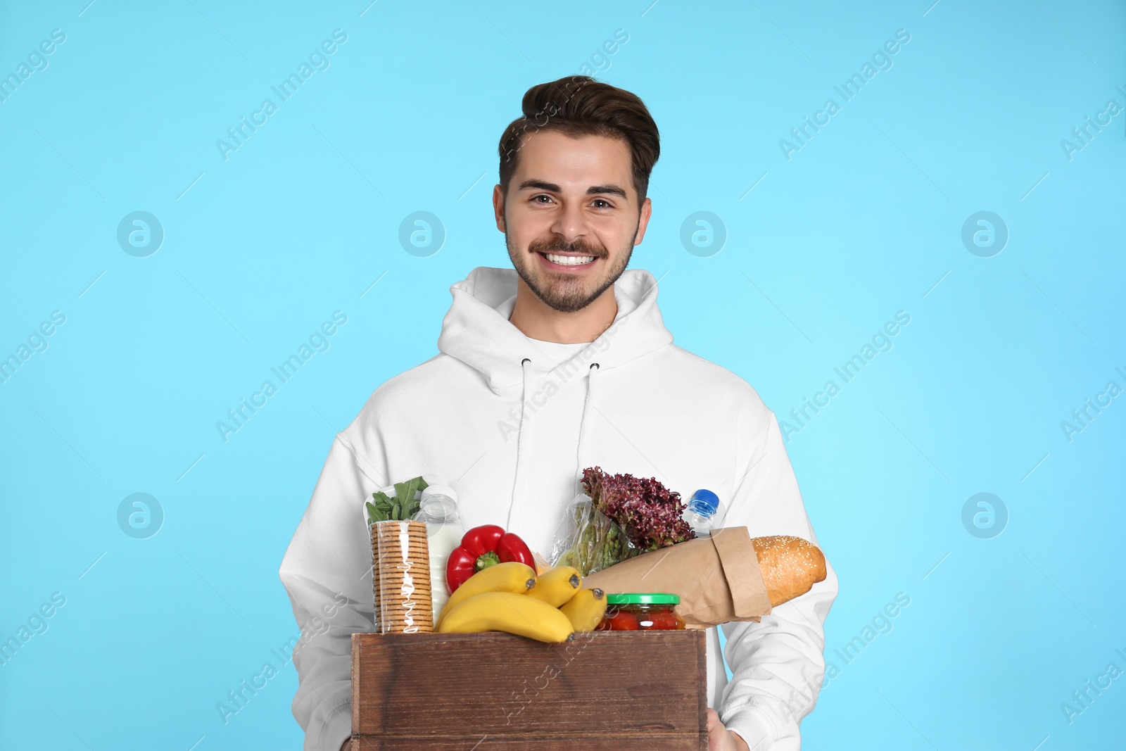 Photo of Young man holding wooden crate with products on color background. Food delivery service