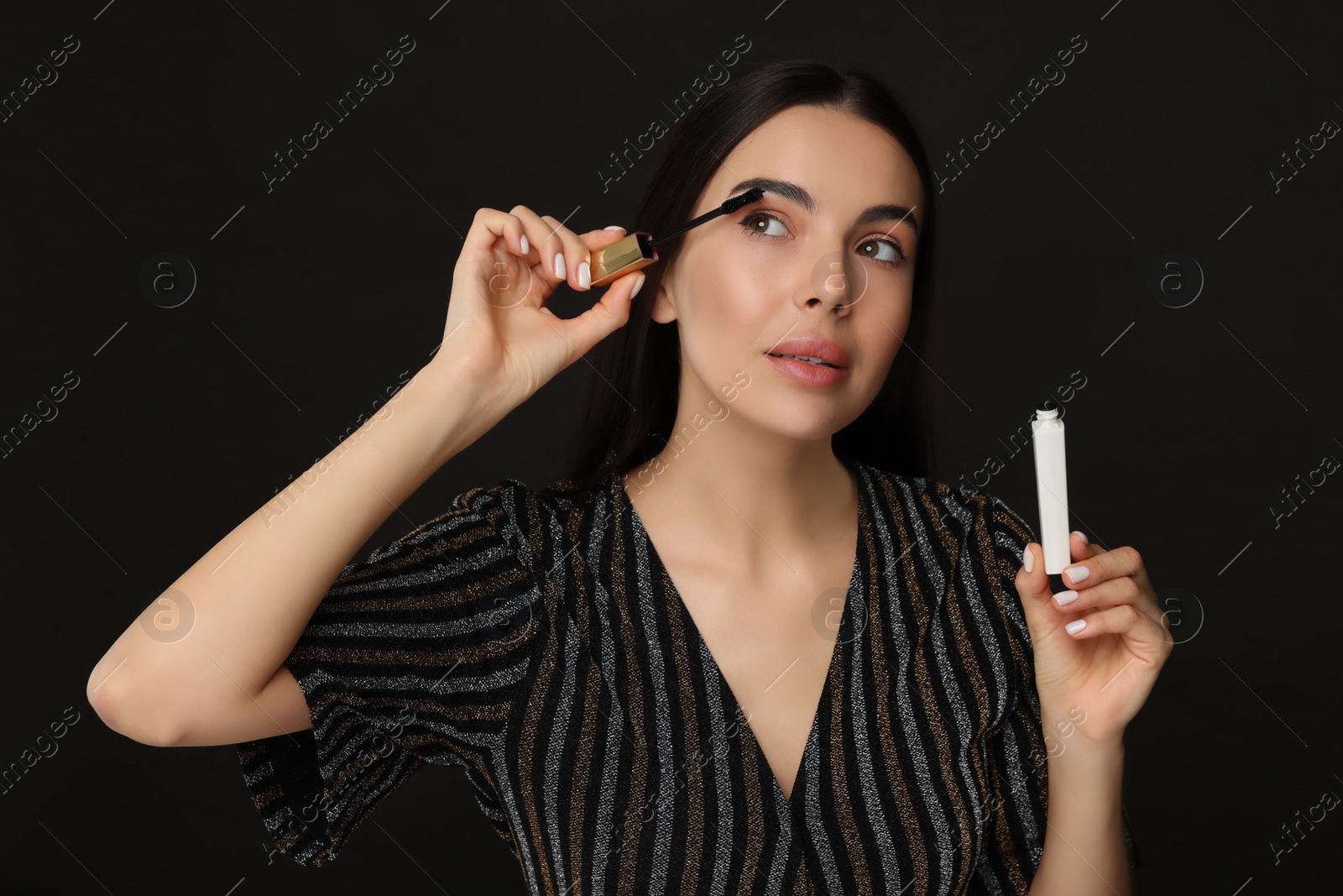 Photo of Beautiful young woman applying mascara on black background