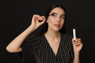Photo of Beautiful young woman applying mascara on black background