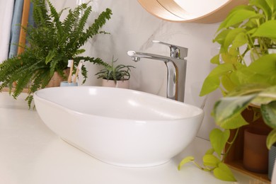 Photo of Bathroom counter with sink, beautiful green houseplants and toothbrushes near white marble wall