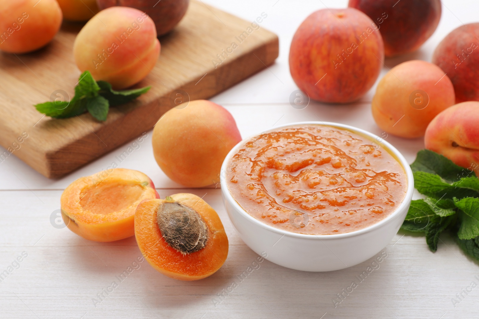 Photo of Apricot puree in bowl and fresh fruits on white wooden table