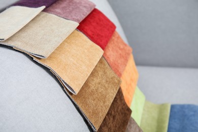 Photo of Catalog of colorful fabric samples on grey sofa, closeup