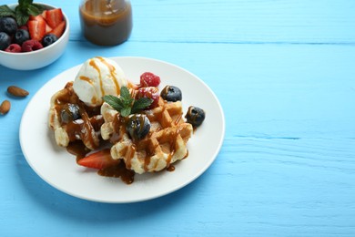 Delicious Belgian waffles with ice cream, berries and caramel sauce on light blue wooden table, space for text