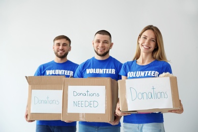 Photo of Young volunteers holding boxes with donations for poor people on light background