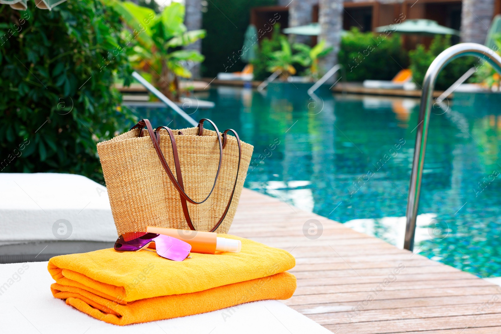 Photo of Wicker bag with beach accessories on sunbed near outdoor swimming pool, space for text. Luxury resort