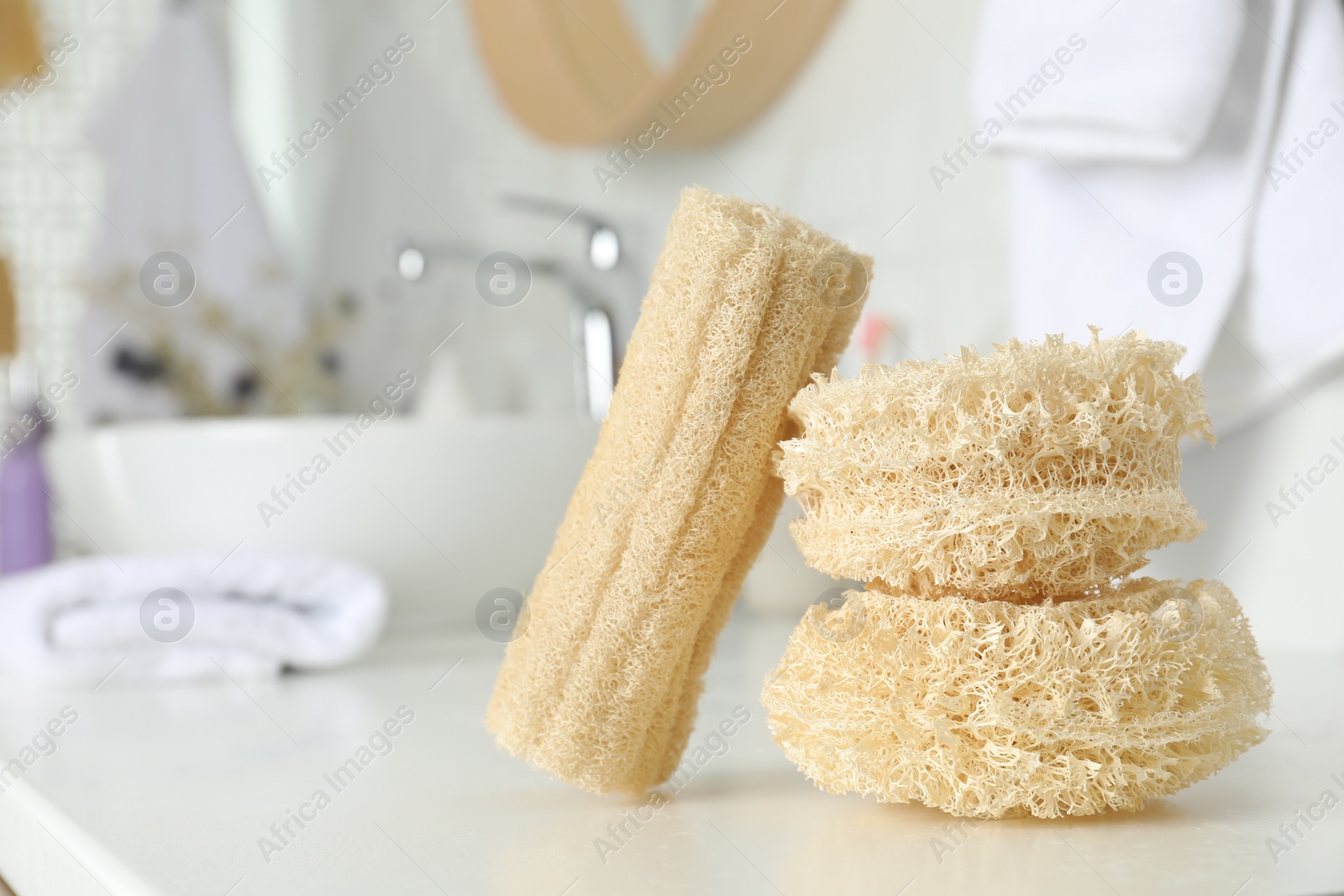 Photo of Natural loofah sponges on table in bathroom. Space for text
