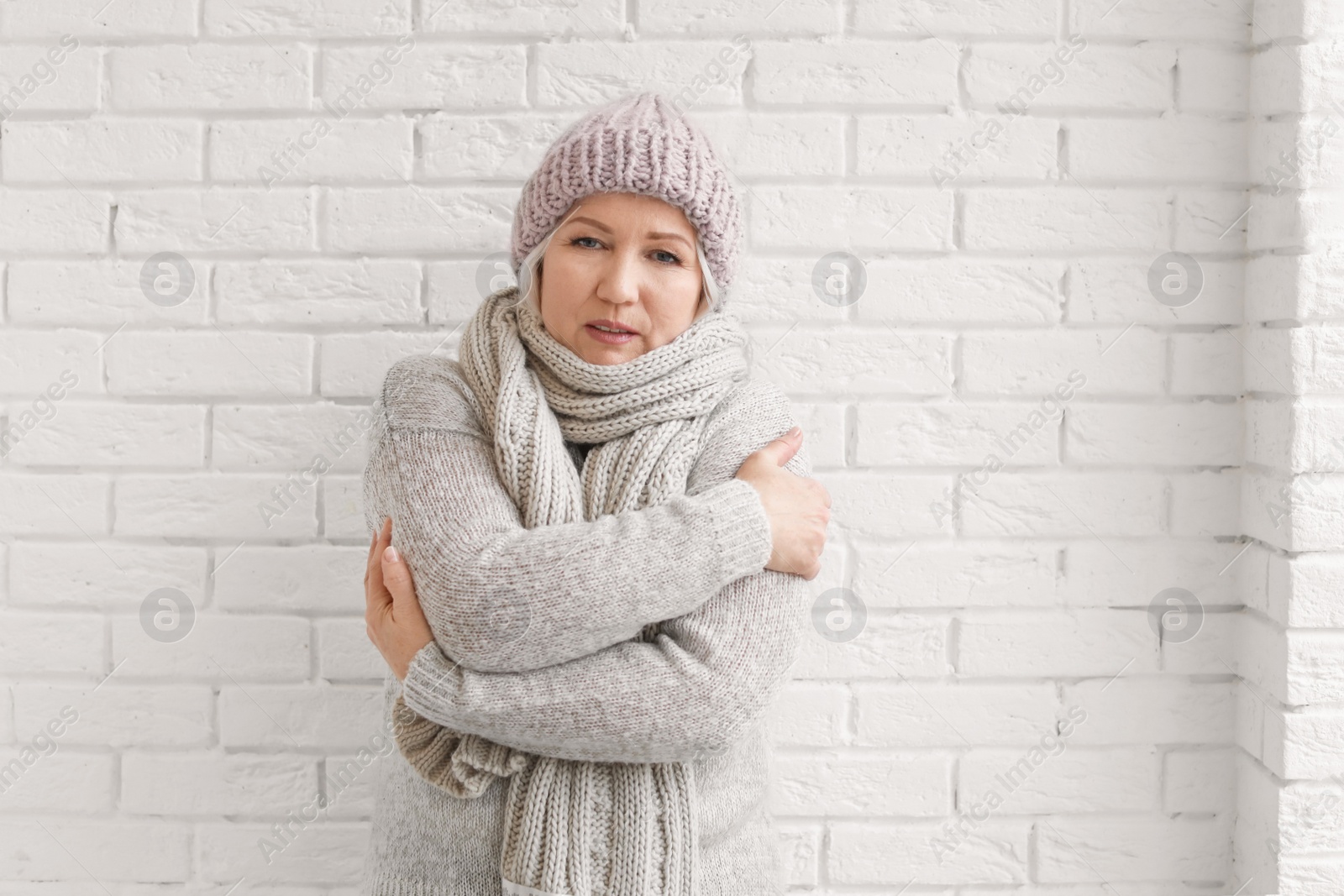 Photo of Mature woman in warm clothes suffering from cold on brick background