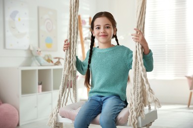 Photo of Cute little girl playing on swing at home