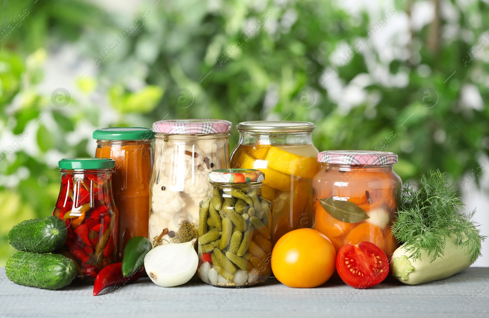Photo of Fresh vegetables and jars of pickled products on wooden table