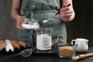 Photo of Woman adding baking powder into measuring cup at black wooden table, closeup