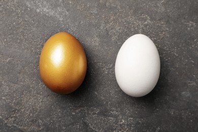 Golden egg and ordinary one on black table, flat lay