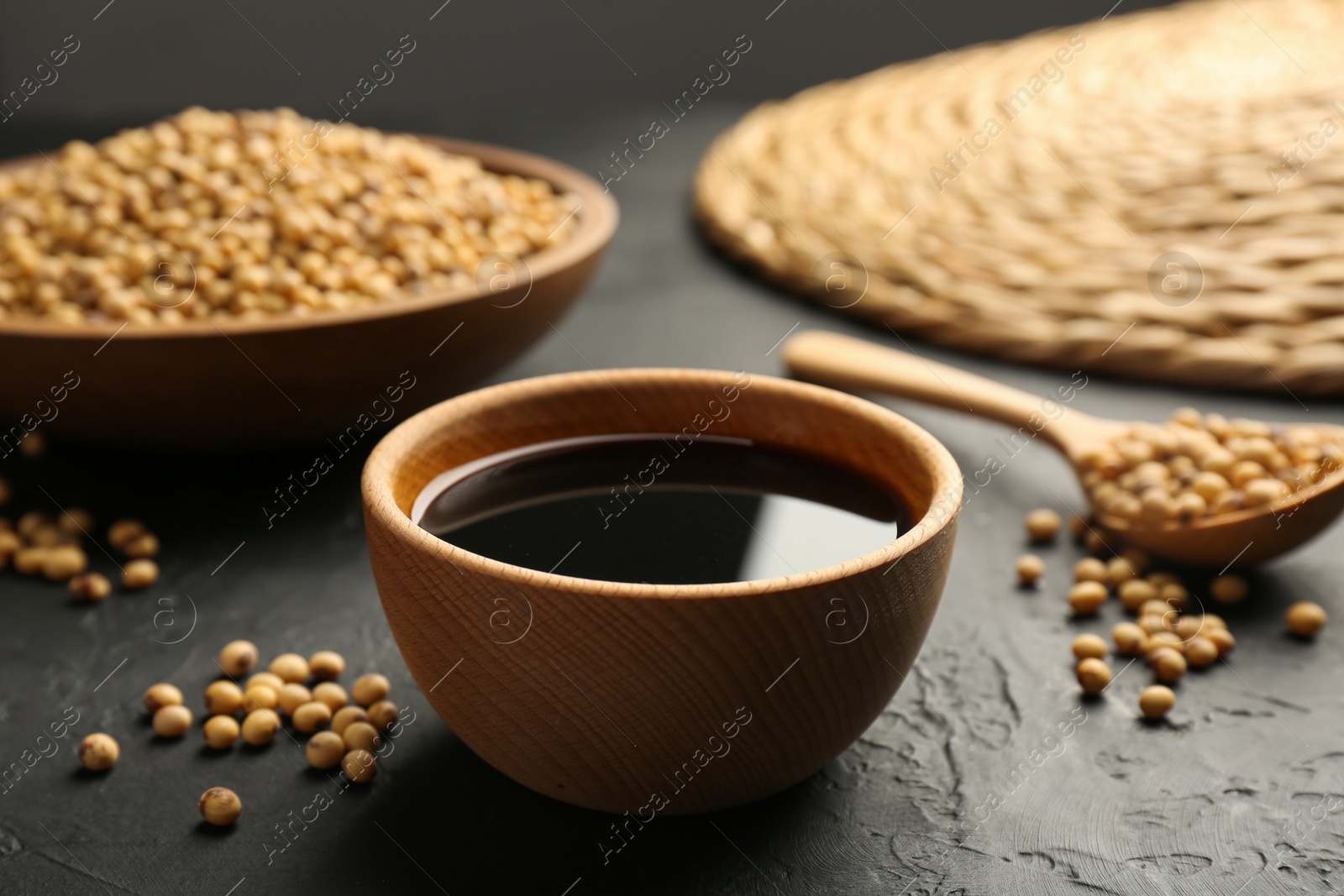 Photo of Tasty soy sauce in bowl and soybeans on black table, closeup