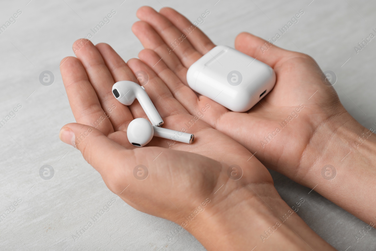 Photo of Woman with wireless earphones and charging case at light table, closeup