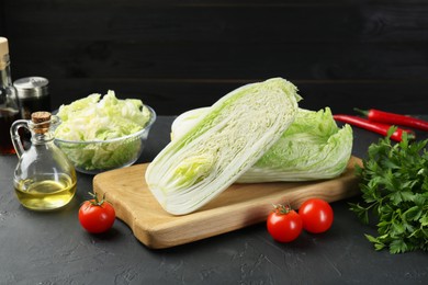 Photo of Fresh Chinese cabbages, tomatoes, parsley and oil on black textured table