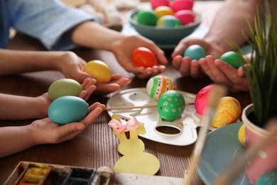Photo of Father, mother and their child painting Easter eggs at wooden table, closeup