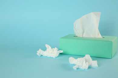 Photo of Used paper tissues and box on light blue background. Space for text