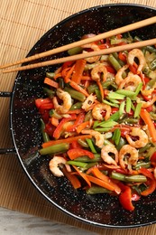 Photo of Shrimp stir fry with vegetables in wok and chopsticks on wooden table, top view